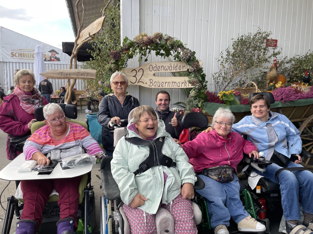 Gruppe mit vier Rollstuhlfahrern auf dem Odenwalder Bauernmarkt lachen in die Kamera