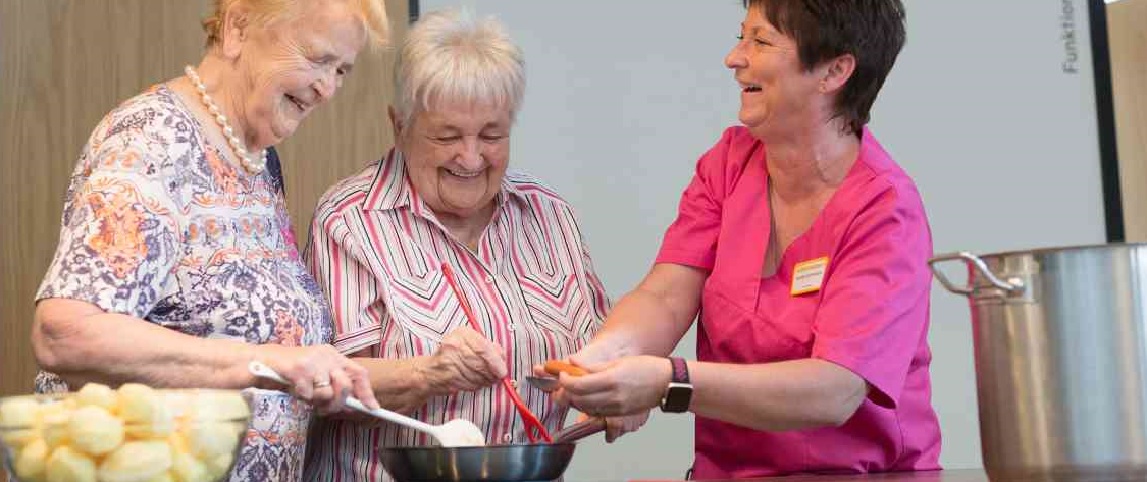 zwei Seniorinnen bereiten unter Anleitung Essen zu