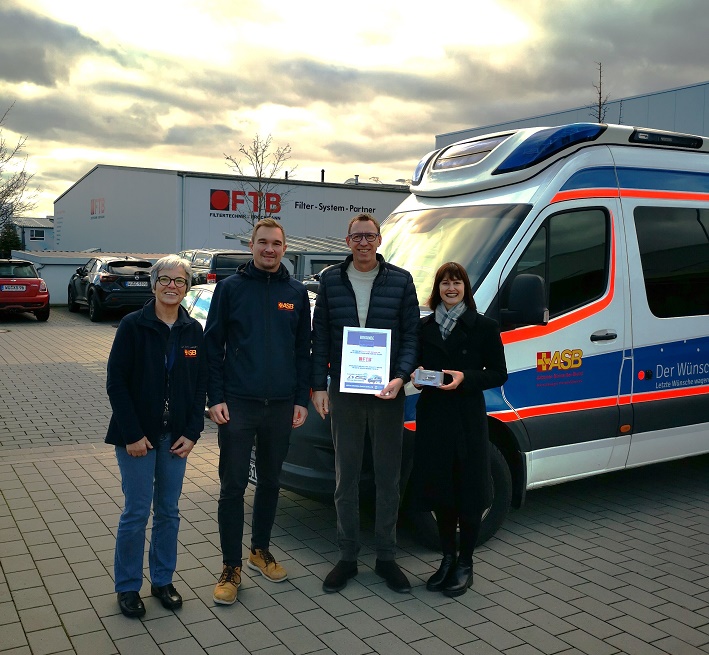 Spendenübergabe Firma Brockmann vier Personen mit Symbolcheck stehen vor Wünschewagen